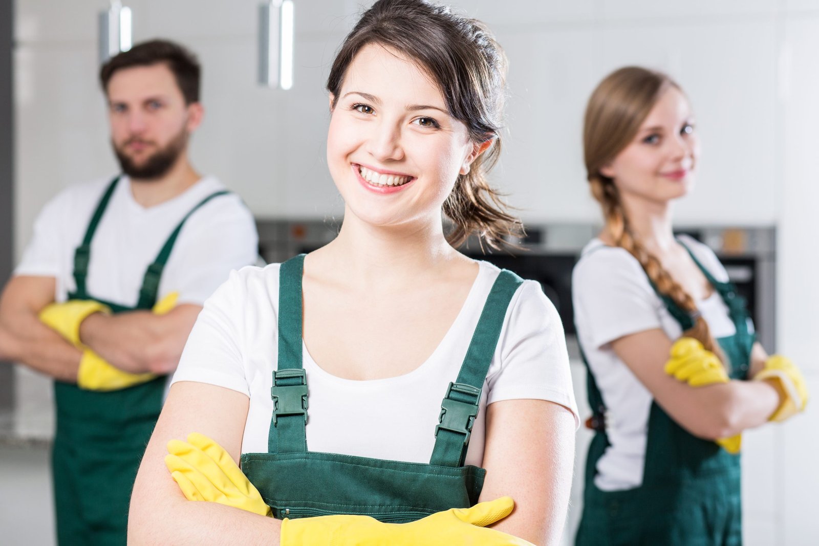 Happy young girl working as a housekeeping. Behind her two colleagues in uniforms