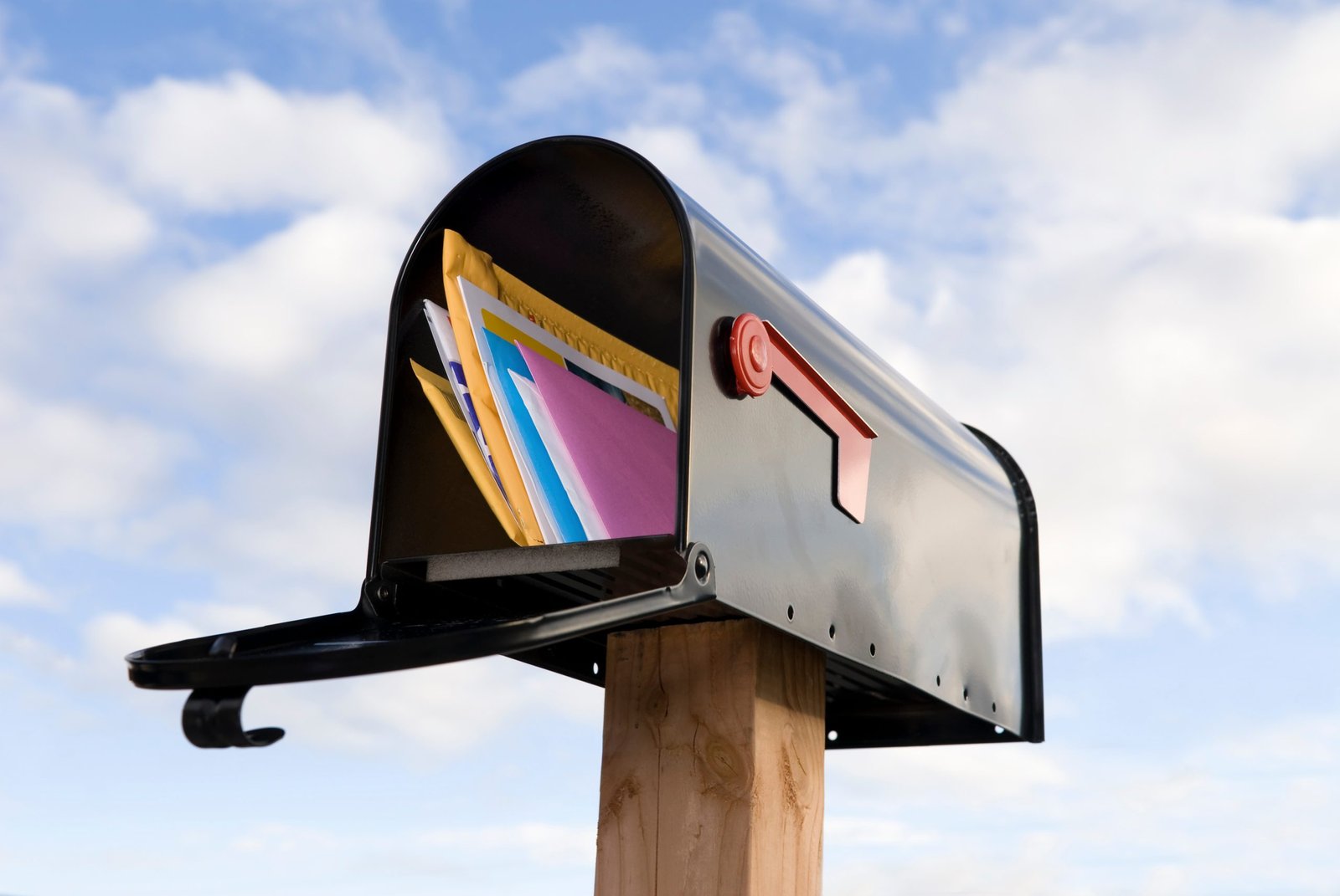A mailbox full of mail against a blue and puffy white cloud sky